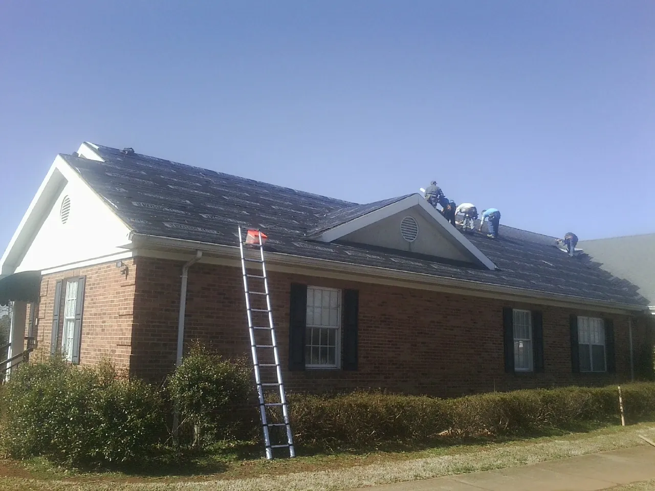 Crew tearing shingles off a brick ranch roof with a ladder set — Emergency Roof Repair work by our crew in Hopkinton
