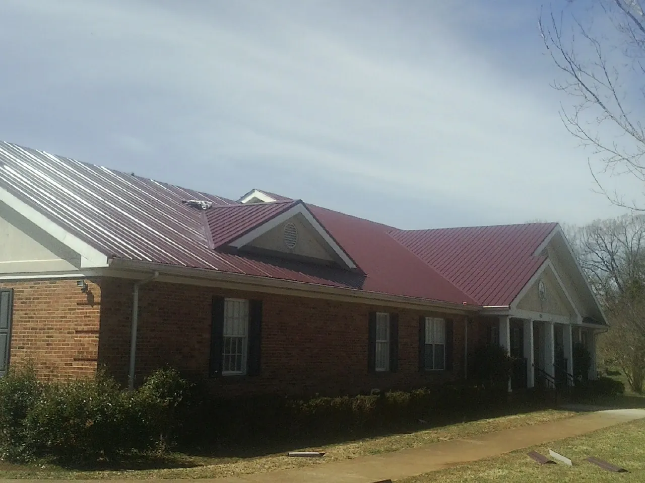Red metal roof with gabled entries on a long brick building, from a Hail Damage Roof Repair job in Hopkinton