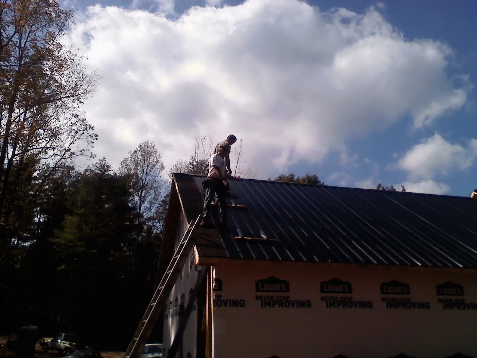 Roofer fastening dark metal panels high against a cloudy sky, from a Roof Inspection job in Hopkinton