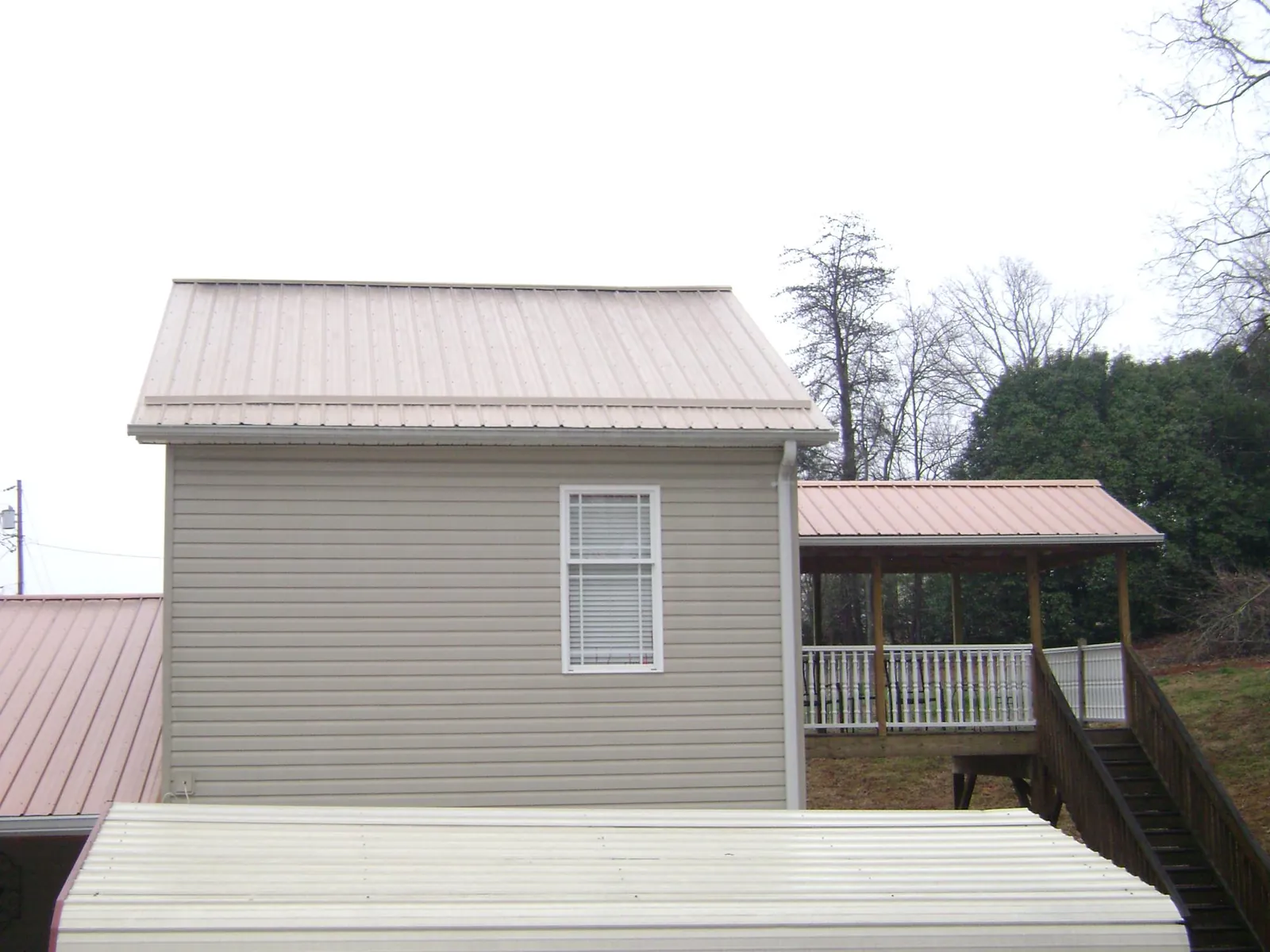 Tan metal roofs on a two story addition and attached porch, from a Roof Replacement job in Hopkinton